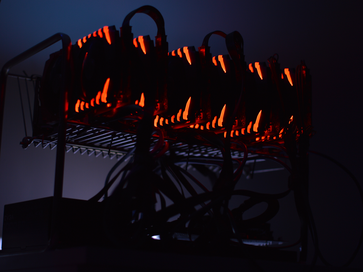 The same mining rig at night, the room completely dark except for the red glow of the GPU LEDs while it mines away